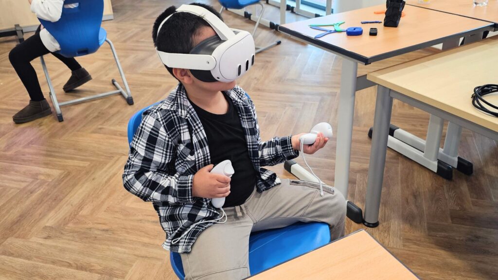 Junge sitzt mit VR-Brille und Controllern auf einem Stuhl und erkundet eine virtuelle Welt