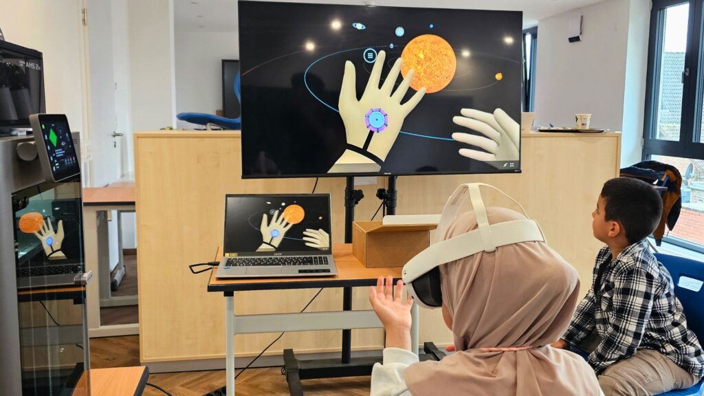 Mädchen mit VR-Brille steuert mit der Hand das Sonnensystem, das auf dem Bildschirm in der TechWerkstatt Setterich zu sehen ist
